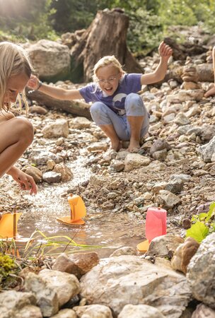 Kinder spielen mit Spielzeugbooten an einem Bachlauf
