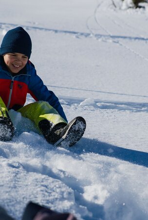 Lachendes Kind in bunter Winterkleidung beim Rodeln im Schnee