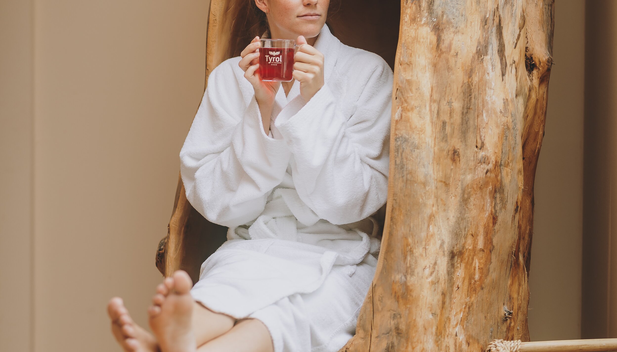 Entspannte Frau im Bademantel trinkt Tee in einem ausgehöhlten Baumstamm.