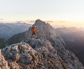 Wanderer auf felsigem Berggipfel bei Sonnenaufgang
