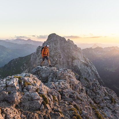 Wanderer auf felsigem Berggipfel bei Sonnenaufgang