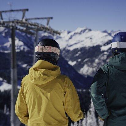 Zwei Skifahrer blicken auf verschneite Berge und Gondel