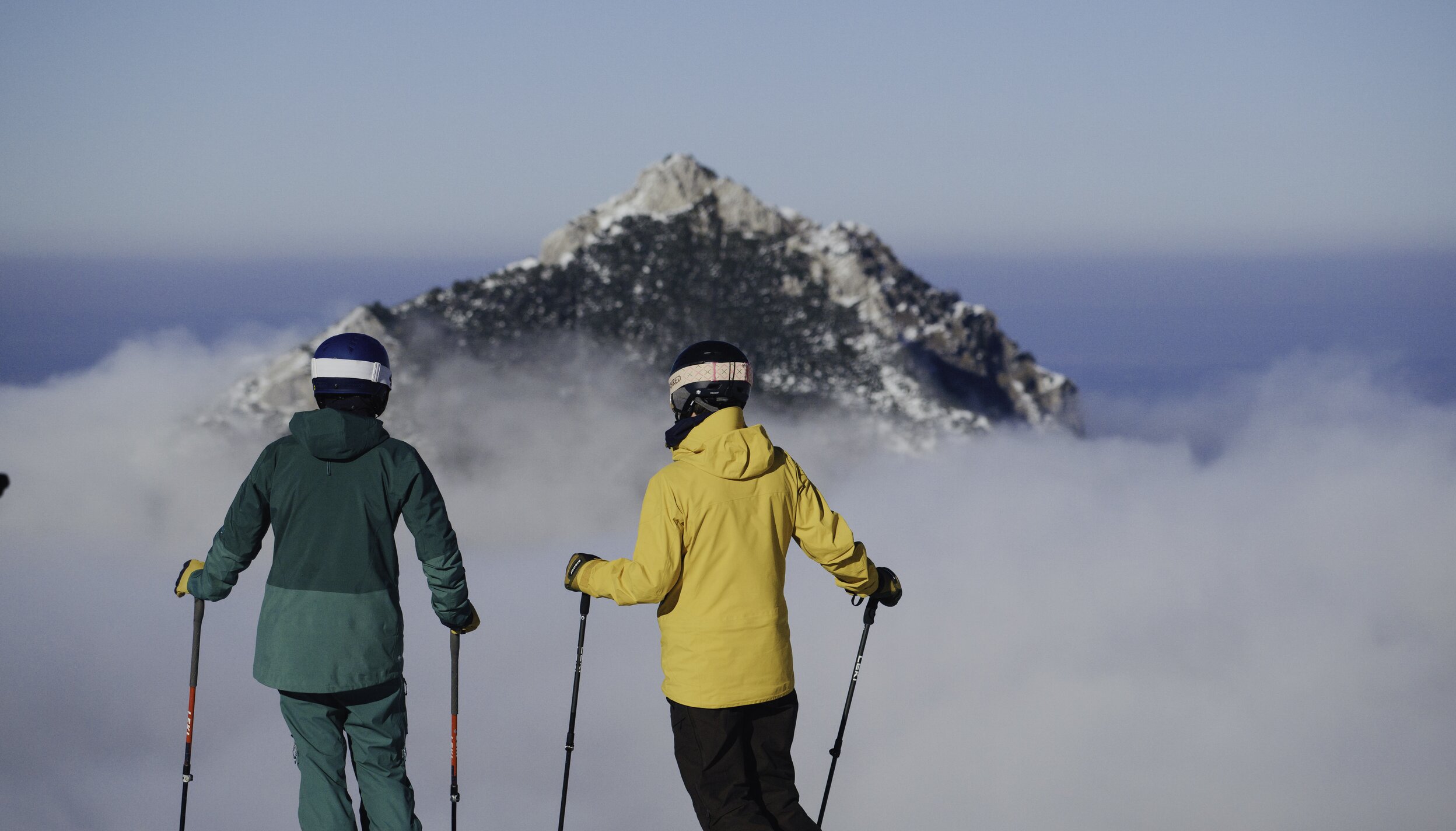 Skifahrerpaar vor schneebedecktem Berg über Wolkenmeer